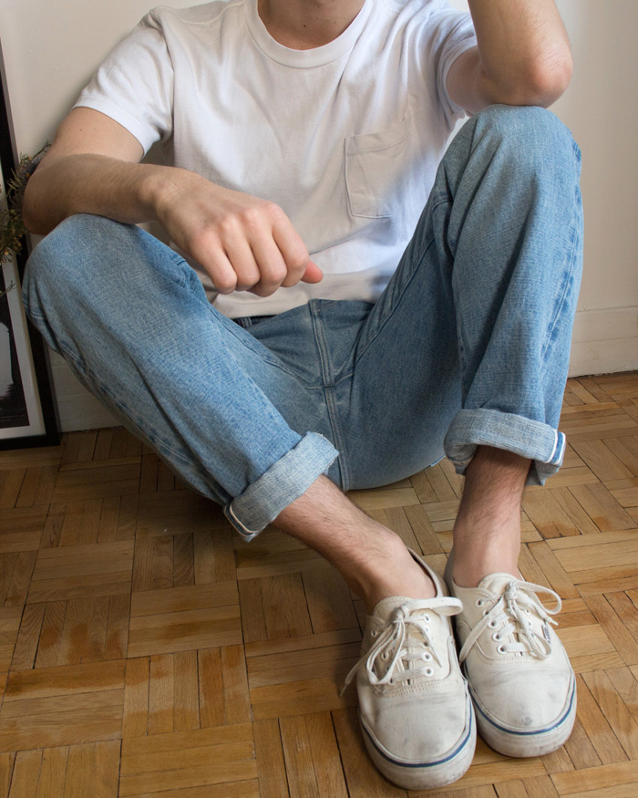 Homme assis en jean délavé bleu ciel sneakers blanches et t-shirt blanc