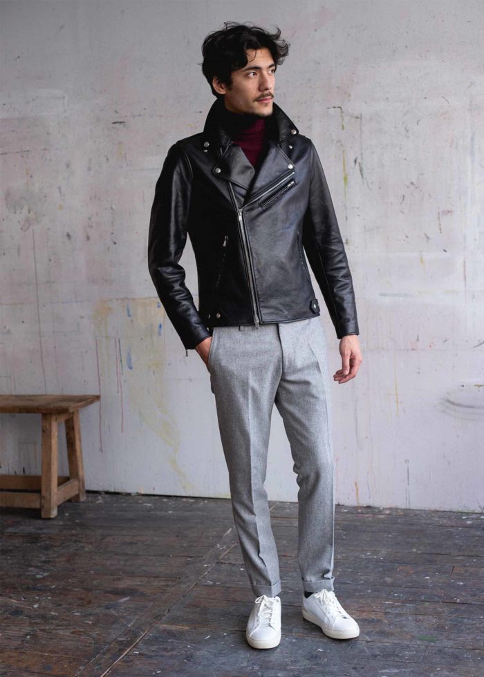 Homme en blouson en cuir noir, pull col roulé bordeaux, et pantalon en laine gris.