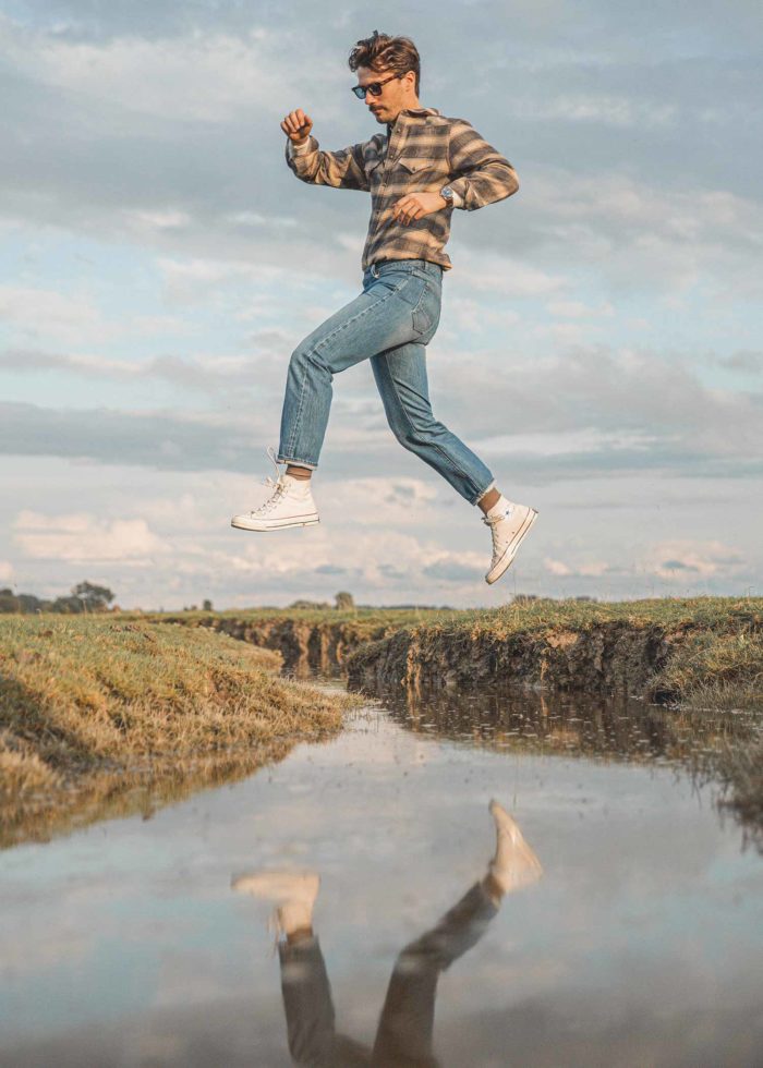 Homme en jean sautant par-dessus une rivière.